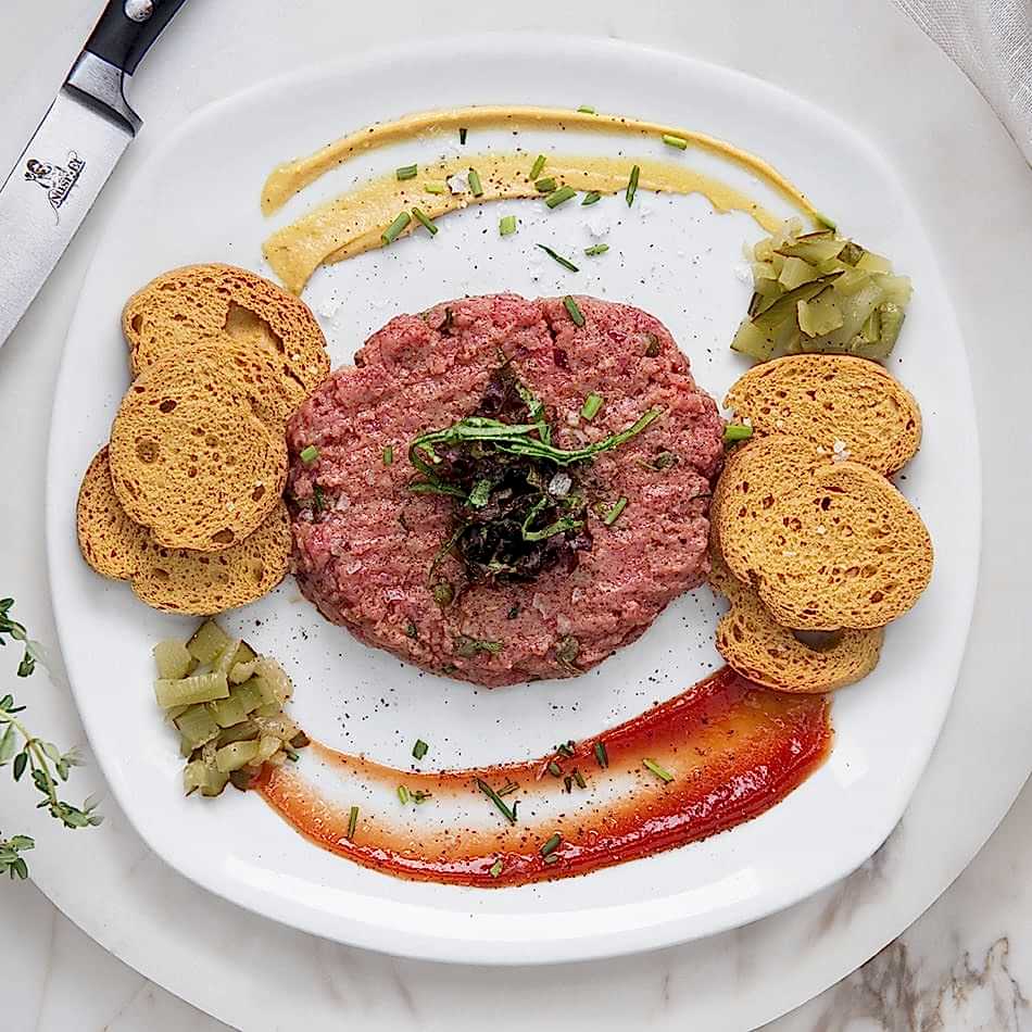 Steak tartare featuring hand-cut beef with capers, chili sauce, cognac, and crispy potatoes,