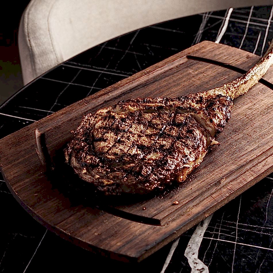 Highly marbled Wagyu Tomahawk ribeye, mustard-marinated and served bone-in, offering a rich, shareable steak experience.