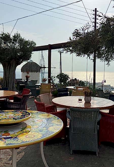Outdoor dining area at Nusret Mykonos overlooking the Aegean Sea, featuring colorful Mediterranean-inspired tables and chairs.