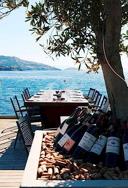 Seaside dining at Nusr-Et Yalıkavak, featuring a wine display under an olive tree with scenic views of the Aegean Sea, perfect for a luxurious meal.